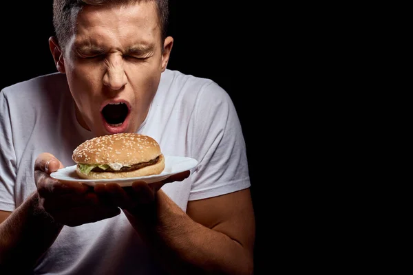 Siyah arka planda hamburger tabağı olan beyaz tişörtlü bir adam fast food manzarası çizdi. — Stok fotoğraf