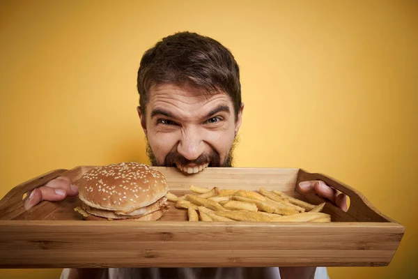 Mężczyzna z drewnianą paletą fast food hamburger frytki dieta spożywcza zbliżenie — Zdjęcie stockowe