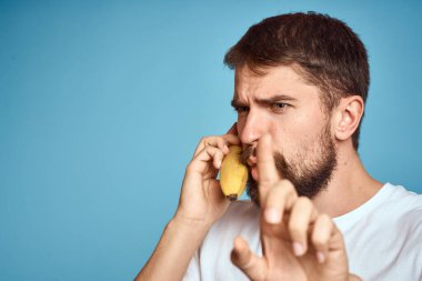 Muzlu bir adam, beyaz bir tişörtle mavi arka planda telefonla iletişim kurarken yakalanır.