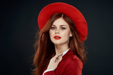 Kırmızı dudaklı güzel bir kadın ceketinde şapkası olan zarif stil cazibesi koyu tenli arka planda.