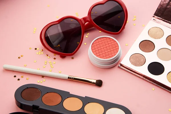 Göz falı aksesuarlar, boncuklar makyaj fırçaları pembe arka planda profesyonel kozmetik ürünleri koleksiyonu.