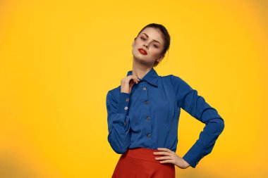 Mavi gömlekli çekici bir kadın, elleri ve kırmızı eteği ile işaret ediyor sarı arka plan portresi kesilmiş.