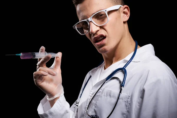 Medico con liquido in una siringa su uno sfondo nero e uno stetoscopio intorno al collo vista ritagliata — Foto Stock