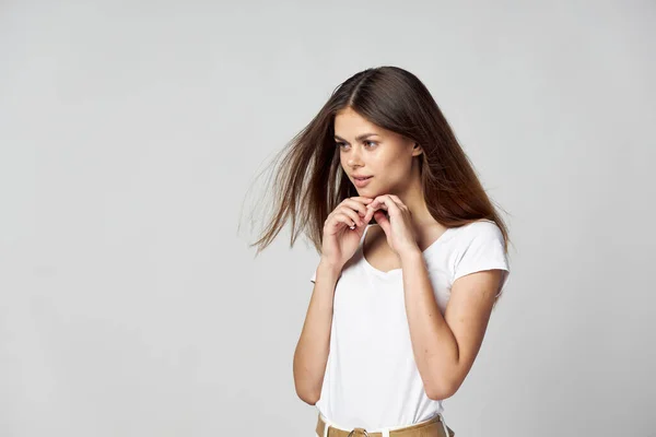 Beautiful woman with loose hair and a white t-shirt holds her hands near her face and looks to the side — Stock Photo, Image