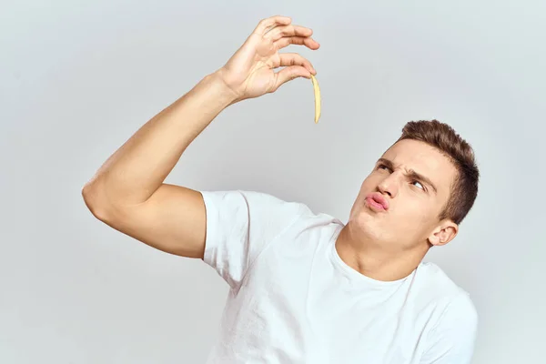Συναισθηματική άνθρωπος κρατώντας πατάτες θερμίδες fast food φως φόντο λευκό t-shirt περικοπή άποψη — Φωτογραφία Αρχείου