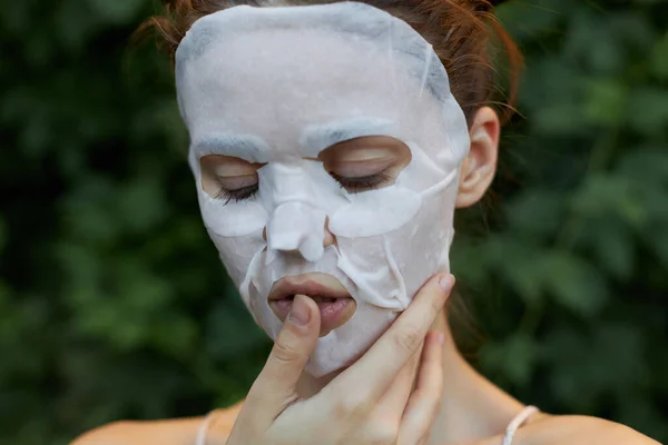 Portret van een vrouw anti-aging masker houdt een vinger dicht bij de lippen en gesloten ogen blote schouders bladeren op de achtergrond — Stockfoto