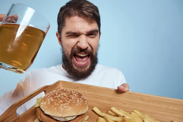 Neşeli adam bira kupa hamburger patates kızartması fast food diyet mavi arka plan yakın plan — Stok fotoğraf