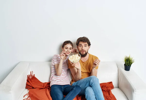 interested man and woman with popcorn on sofa orange plaid and flower in a pot