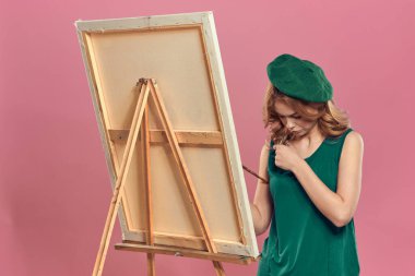 Kadın sanatçı yeşil bereli sehpa fırçası çizim dersleri pembe arka plan