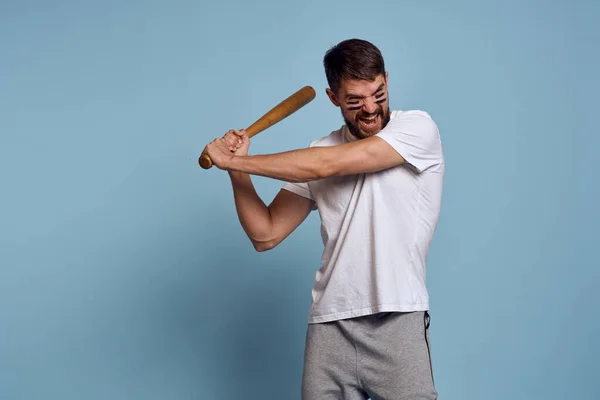 Hombre emocional con un bate en la mano sobre un fondo azul y maquillaje en su cara negro líneas de energía camiseta de béisbol — Foto de Stock