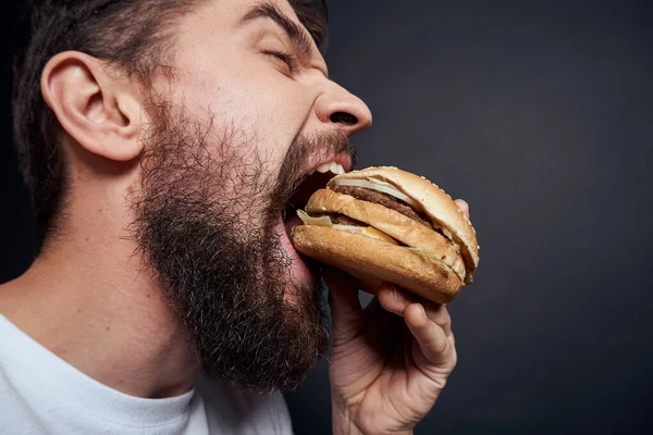 Uomo mangiare hamburger fast food ristorante Gourmet mangiare sfondo scuro — Foto Stock