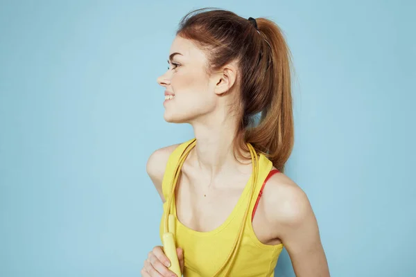 Sportieve vrouw met een springtouw gele tank top oefening gymnastiek blauwe achtergrond — Stockfoto