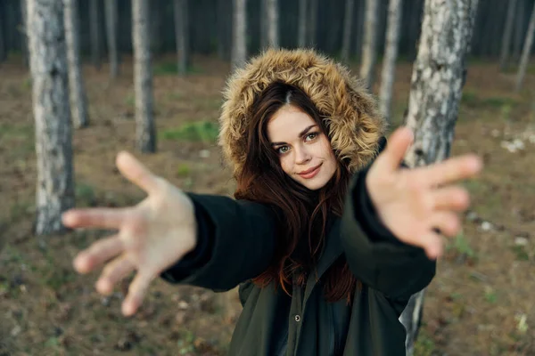 Egy fekete kabátos nő kinyújtotta a karját a természet felé az erdő hátterében. — Stock Fotó