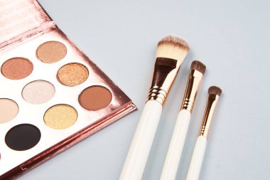 Göz farı aksesuarları, makyaj fırçaları, gri arka planda profesyonel kozmetik ürünleri.