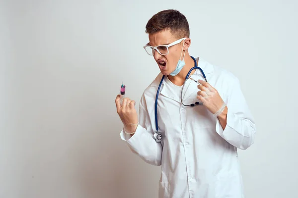 Médico com um estetoscópio em óculos segura uma seringa em suas mãos em uma vista lateral de fundo leve — Fotografia de Stock