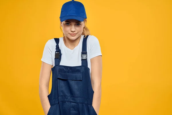 Kvinna i arbetande uniform blå mössa leverera kurir service gul bakgrund — Stockfoto