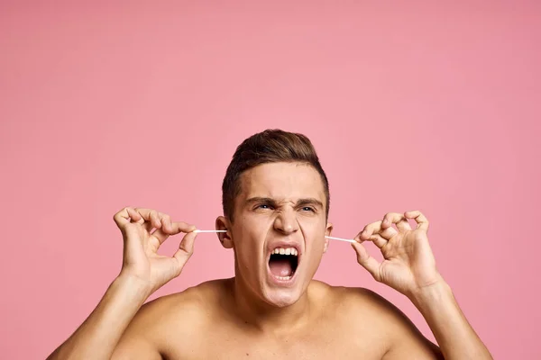 Känslomässig man med öronklubbor i händerna på rosa bakgrund känslor beskärd utsikt över naken bål — Stockfoto
