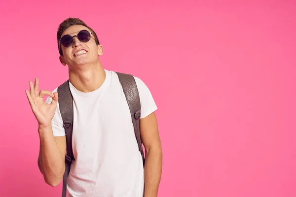 Portrait of a man in a white T-shirt and with a backpack on his back sunglasses pink background model — Stock Photo, Image