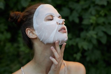 Güzel bir kadın yaşlanmayı önleyen bir maske takar. Elini yüzüne yaklaştırır. Başını geriye yaslar.