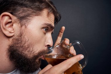 Beyaz tişörtlü, bir kupa birası olan bir adam. Duyguları olan, koyu tenha bir arka planda sarhoş bir adam.