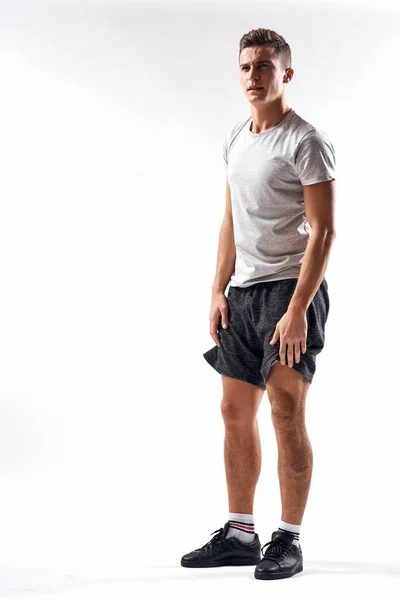 Een sportman in shorts en een full-length T-shirt doet oefeningen op een lichte achtergrond — Stockfoto