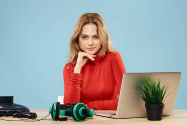 Dizüstü bilgisayar kulaklığının önündeki masada oturan bir kadın çevrimiçi yaşam tarzı mavi arka planda oynuyor.