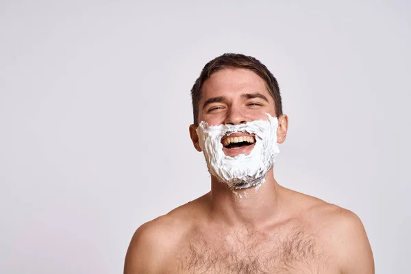 Όμορφος άντρας με λευκό αφρό ξυρίσματος στο πρόσωπό του και καθαρό δέρμα με ξυράφι να περιποιείται γυμνούς ώμους. — Φωτογραφία Αρχείου