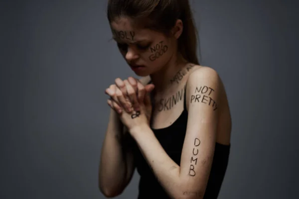怒气冲冲的女人在身上刻着愤怒的文字，用手触摸着灰色背景的攻击行为 — 图库照片