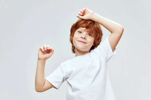 Glada rödhåriga pojke hålla händerna på huvudet vit t-shirt kfk grå bakgrund — Stockfoto