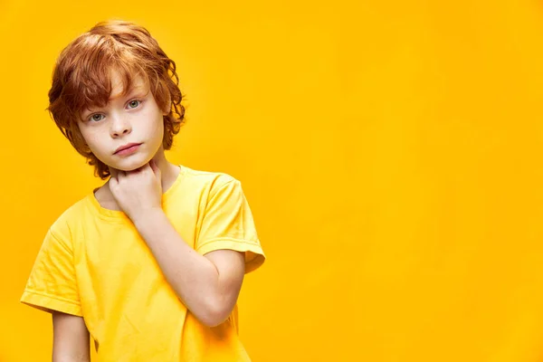 Retrato de un niño lindo con vista frontal de pelo jengibre en una camiseta amarilla expresión facial interesada —  Fotos de Stock