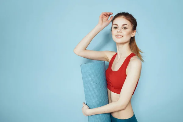 Sportieve vrouw in rode tank top mat voor workout oefeningen lifestyle blauwe achtergrond — Stockfoto