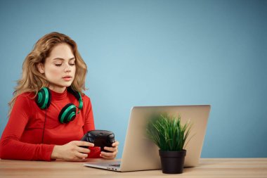 Dizüstü bilgisayar kulaklığının önündeki masada oturan bir kadın çevrimiçi yaşam tarzı mavi arka planda oynuyor.