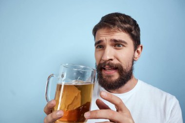 Beyaz tişörtlü, bira kupalı, sarhoş, mavi arka planlı neşeli bir adam.