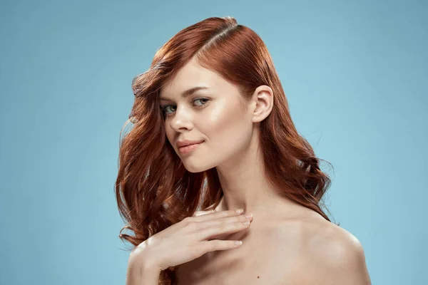 Piękna kobieta kręcone długie włosy gładka fryzura nagie ramiona kosmetyki opieki niebieskie tło — Zdjęcie stockowe