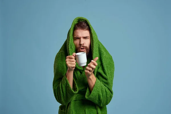 Frozen man in a warm robe with a cup of hot drink on a blue background cropped view — Stock Photo, Image