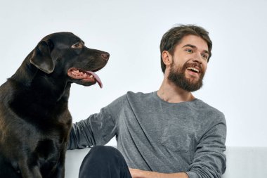 Erkek sahibi kanepede köpekle oynuyor. Eğlenceli ışık odası arkadaşları evcil hayvanı eğitiyor.