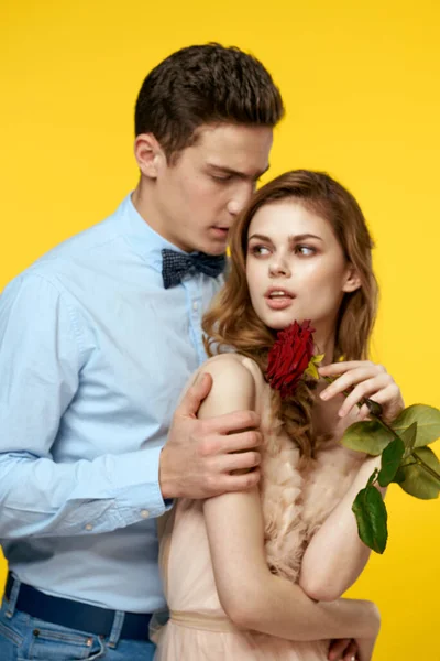 Um jovem casal amoroso com uma rosa vermelha em suas mãos estão abraçando em um fundo amarelo — Fotografia de Stock