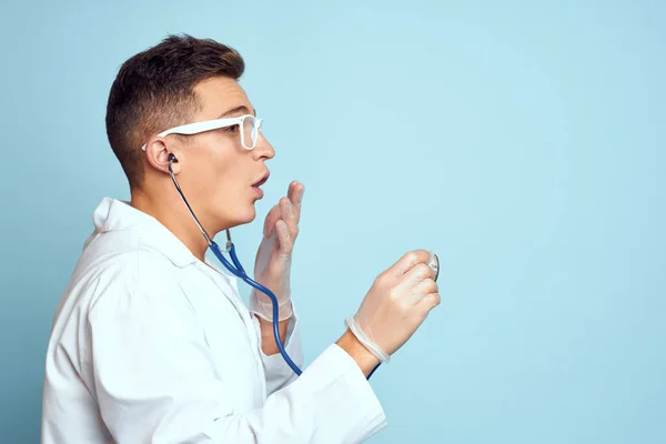 Un travailleur médical en robe de chambre et lunettes tient un stéthoscope dans ses mains sur un fond bleu recadré vue — Photo