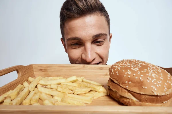 Önünde bir palet dolusu fast food patates kızartması ve yakın plan hamburger yiyen bir adam var. — Stok fotoğraf