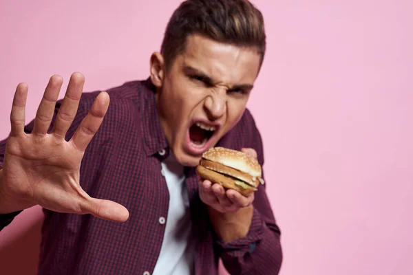 햄버거를 손에 쥐고 패스트푸드를 먹고 있는 배고픈 사람은 핑크 색 배경을 가지고 있다 — 스톡 사진