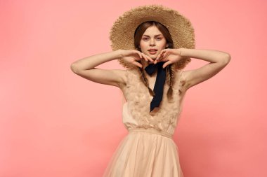 Pembe arka planda siyah kurdeleli şık elbiseli ve şapkalı bir kadın model duygularının eğlenceli görüntüsünü kırptı.