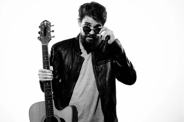 Un homme tient une guitare dans ses mains veste en cuir noir lunettes sombres performance musique fond clair — Photo