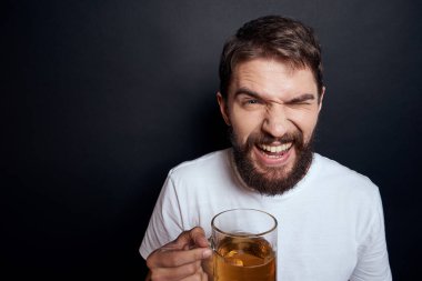 Beyaz tişörtlü, bir kupa birası olan bir adam. Duyguları olan, koyu tenha bir arka planda sarhoş bir adam.