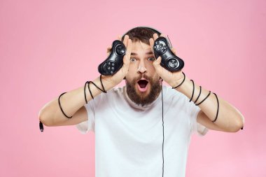 Kulaklıklı, elinde joystickle oyun oynayan, eğlenceli, pembe arka planlı bir adam.