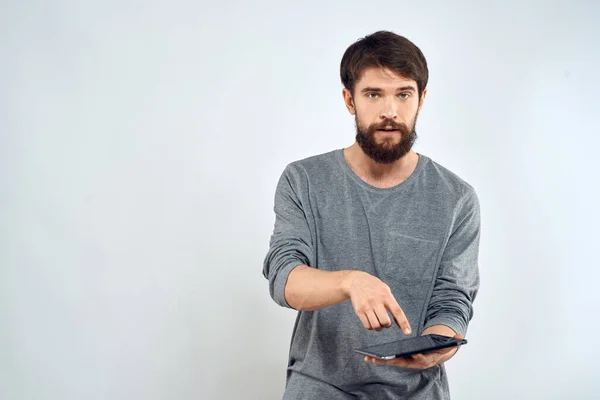 Een man in een grijze trui een tablet in de handen van emoties Internet technologie levensstijl licht achtergrond — Stockfoto