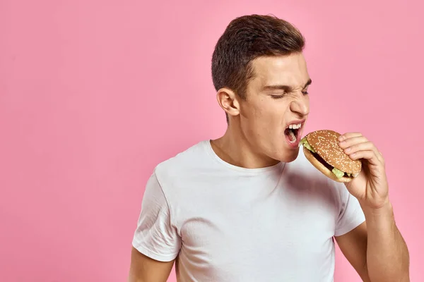 Muž s velkým hamburger na růžovém pozadí kalorie rychlé občerstvení oříznutý pohled kopírovat prostor close-up — Stock fotografie