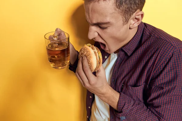 Bir kupa birası ve elinde hamburgerle neşeli bir adam diyet yaşam tarzı sarı arka plan — Stok fotoğraf