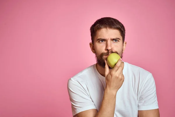 Lindo hombre con una manzana sobre un fondo rosa gestos con las manos recortadas camiseta blanca Copiar espacio — Foto de Stock