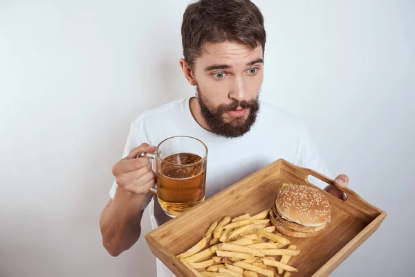 Man met houten dienblad bier mok frietjes en hamburger fast food calorieën model wit t-shirt — Stockfoto