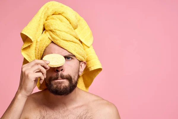 Homem com toalha amarela em sua cabeça esponja limpa cuidados da pele rosa fundo — Fotografia de Stock